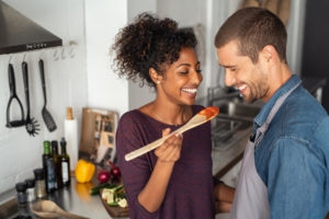 Man and woman in a kitchen. Woman holding a spoon with food