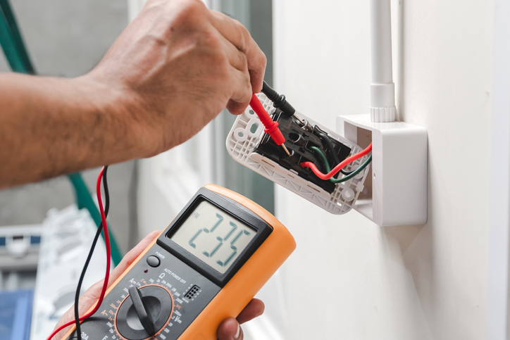 Electrician is using a digital meter to measure the voltage at the power outlet in on the wall, while doing a full service electrical upgrade on a home