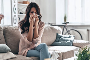 young woman sneezes while sitting on the sofa at home