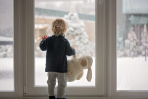 Child standing in front of a window with snow outside