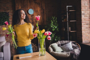 Young woman enjoying the beauty of spring flowers while arranging a bouquet in her stylish apartment