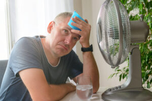 house is too hot, man is sweating in front of fan