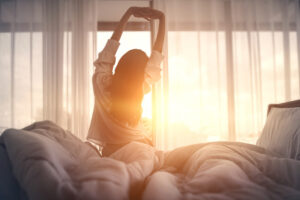 Happy woman stretching in bed after waking up.